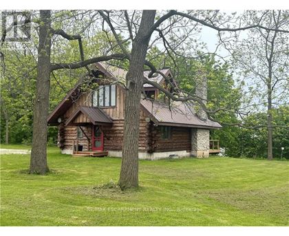 A log cabin sits in a grassy field with trees in the background.