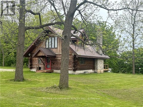 A log cabin sits in a grassy field with trees in the background.
