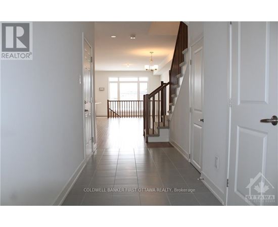 A hallway with white walls and a tiled floor leads to a bright room with a window.