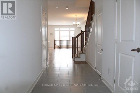 A hallway with white walls and a tiled floor leads to a bright room with a window.