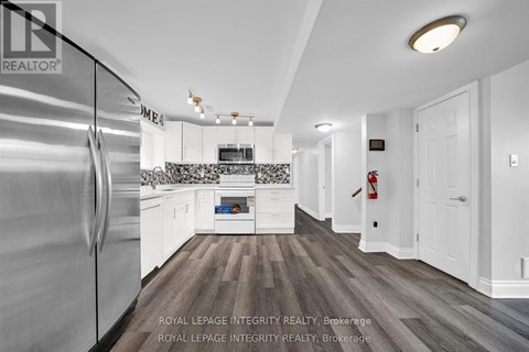 A modern kitchen with a stainless steel refrigerator and wooden flooring.