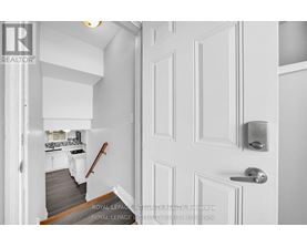 A white door with a silver handle is in the foreground of a photo showing a hallway.