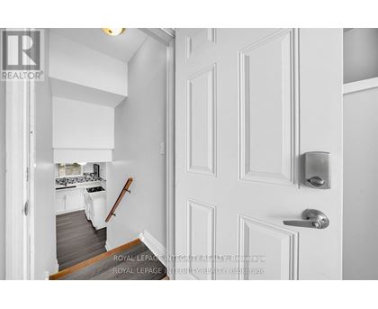 A white door with a silver handle is in the foreground of a photo showing a hallway.