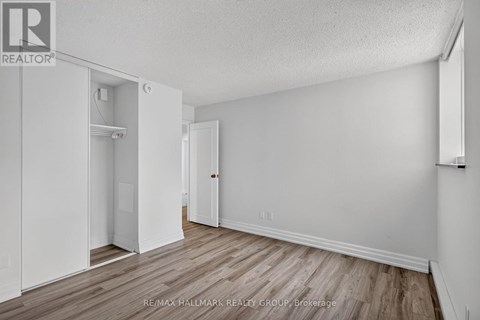 A white bedroom with wood flooring and a closet with a door open.