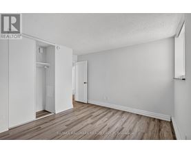 A white bedroom with wood flooring and a closet with a door open.