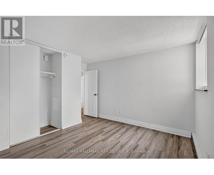 A white bedroom with wood flooring and a closet with a door open.