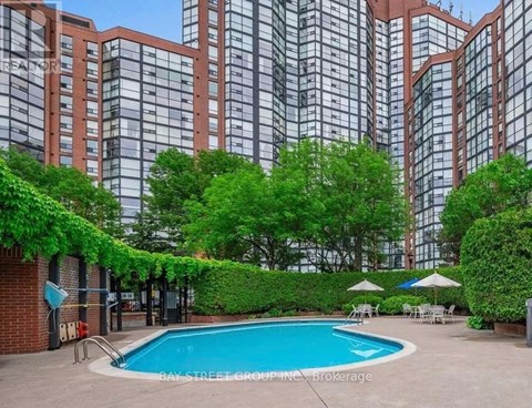 A pool surrounded by greenery and trees in front of a building.