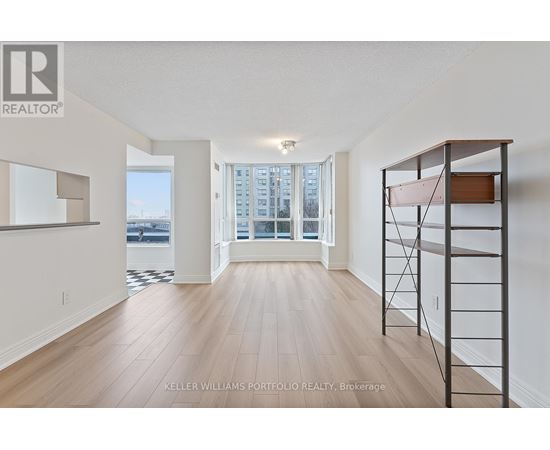 A spacious room with wooden flooring and a large window overlooking a cityscape.