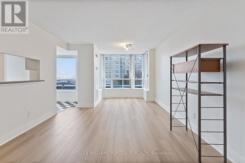 A spacious room with wooden flooring and a large window overlooking a cityscape.
