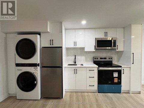 A white kitchen with a washer and dryer on the left and a dishwasher and oven on the right.