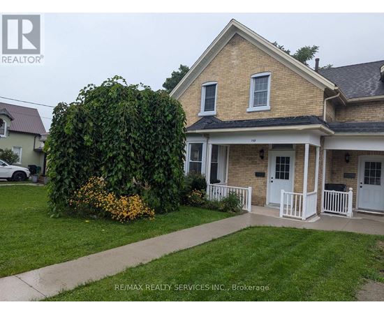 A house with a white front porch and a large green bush in front.