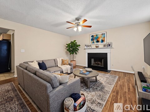 A living room with a grey couch, a coffee table, a fireplace, and a ceiling fan.