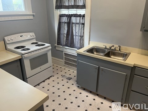 A kitchen with a white stove top oven and a white sink with a silver faucet.