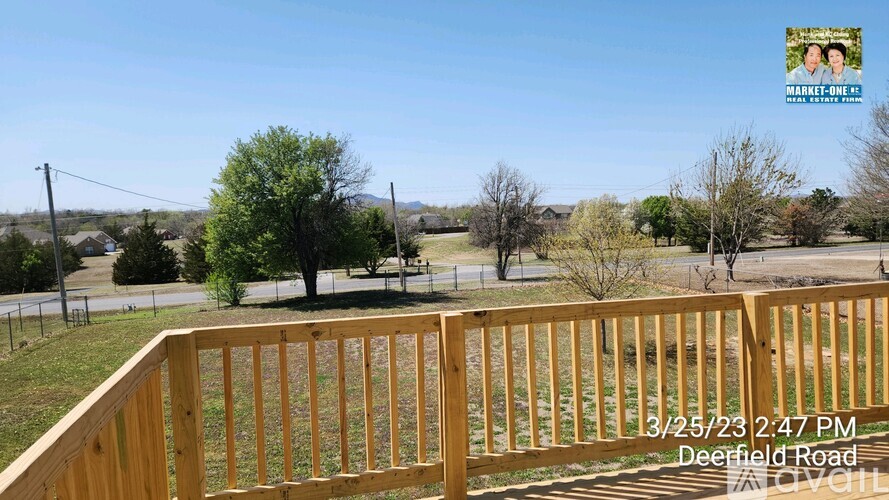 A wooden deck overlooks a grassy area with trees and a clear blue sky.