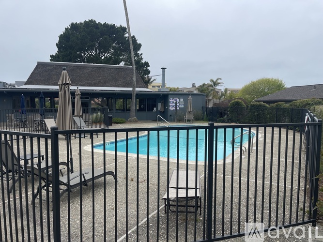 A pool surrounded by a black fence with a patio and umbrella in the background.