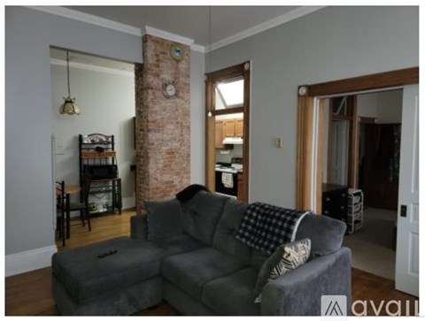 A grey couch with a pillow and a blanket on it in a room with a brick pillar.