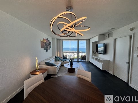 A modern dining room with a wooden table and chairs, a TV, and a view of the ocean through the window.