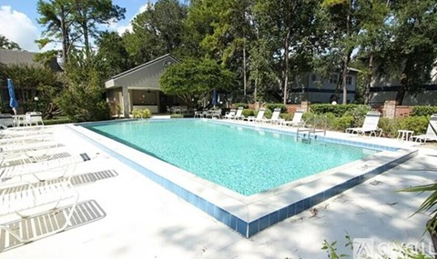 A large swimming pool surrounded by lounge chairs and trees.