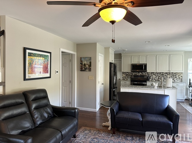 A living room with a black leather couch and a ceiling fan.