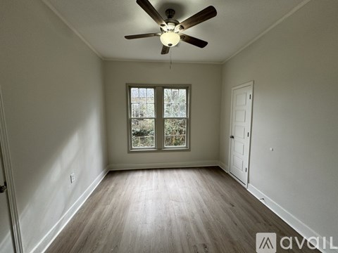 A room with a ceiling fan and a window with a view of trees.