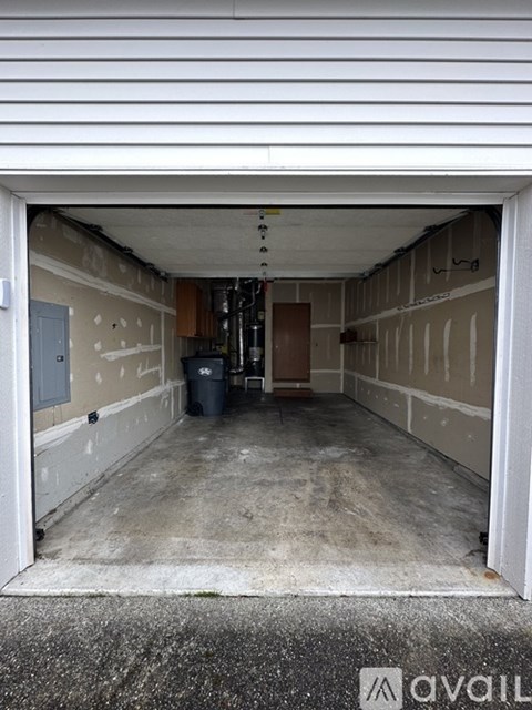 A dirty garage with a door open and a trash can in the middle.