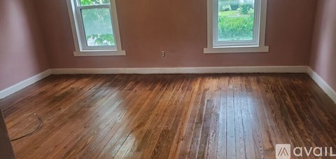 A room with wooden flooring and two windows.
