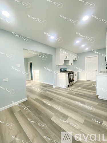 A well-lit, spacious room with wooden flooring and a kitchen area in the background.