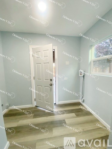 A room with a white door and a window with a view of trees outside.