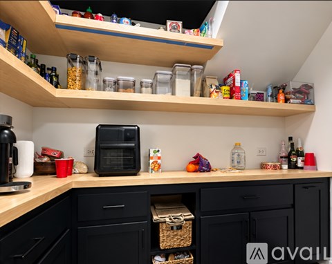 A kitchen with black cabinets and wooden shelves filled with various items.
