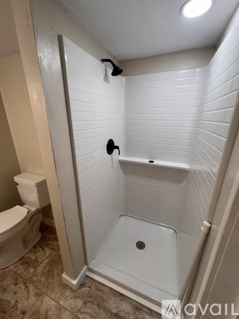 A white tiled shower with a toilet and a towel rack.