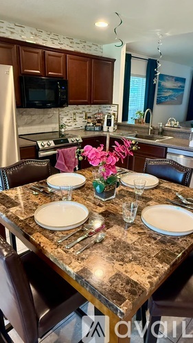 A kitchen with a table set for two with a vase of pink flowers in the middle.