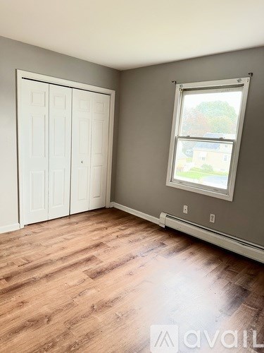 A room with a white door and a window with a view of a tree and a building outside.