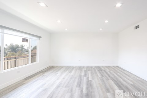 A spacious room with wooden flooring and a large window overlooking a fence.