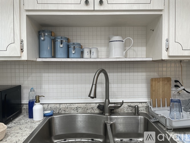 A kitchen with a sink and a shelf with cups and containers.