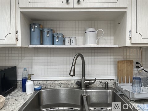 A kitchen with a sink and a shelf with cups and containers.