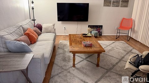 A living room with a white couch, a wooden coffee table, and a television mounted on the wall.