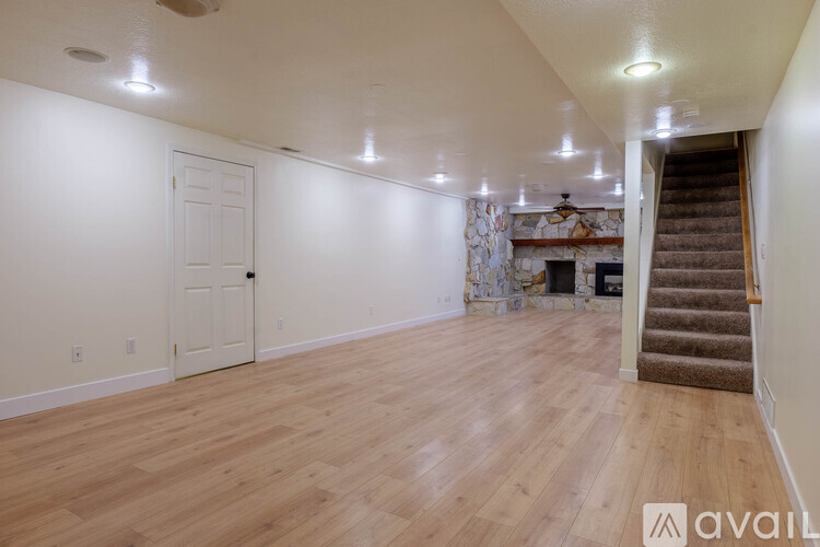 A spacious room with wooden flooring and a staircase on the right side.