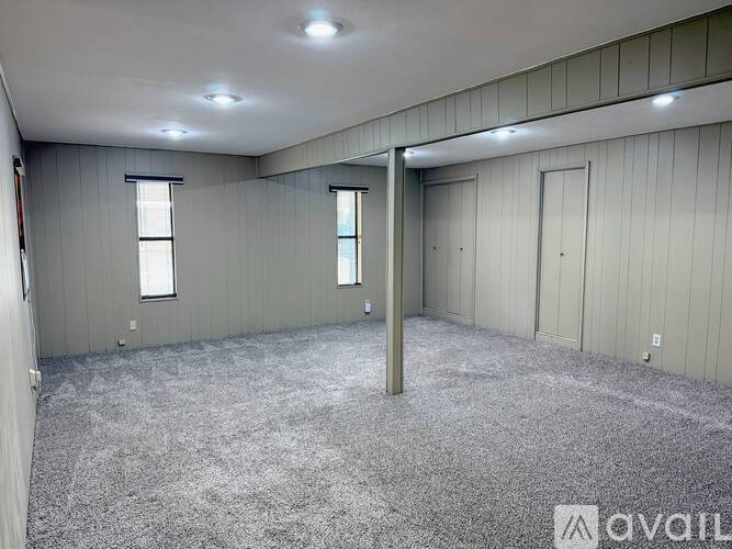 A spacious room with grey carpeting and wooden paneling on the walls.