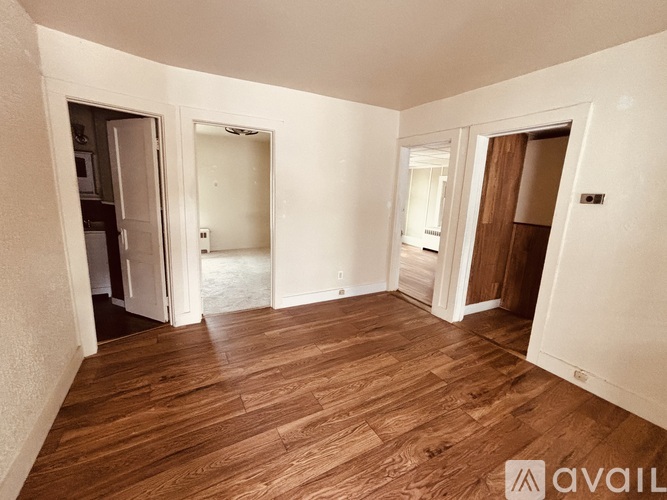 A room with wooden flooring and white walls, with two open doors leading to other rooms.