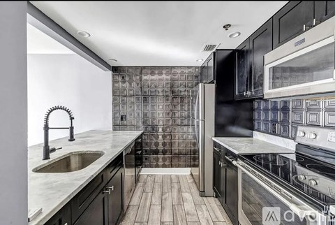 A modern kitchen with black cabinets and a wooden floor.
