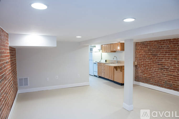 A spacious room with a brick wall and a kitchen area with wooden cabinets.