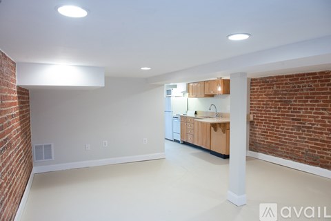 A spacious room with a brick wall and a kitchen area with wooden cabinets.