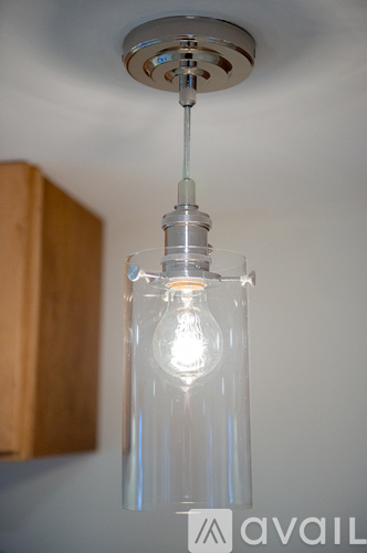 A clear glass pendant light with a lit bulb hanging from a silver metal fixture.