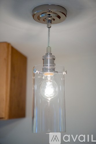 A clear glass pendant light with a lit bulb hanging from a silver metal fixture.