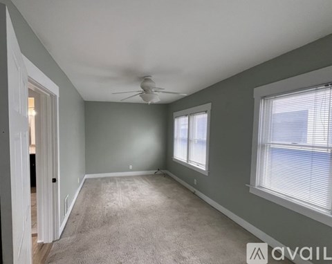 A spacious room with a ceiling fan and two windows.