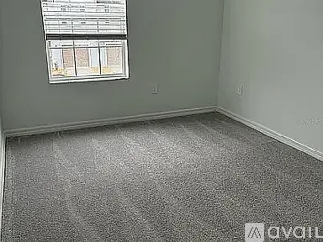 A room with a grey carpet and a window showing a view of a building.