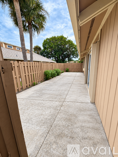 A concrete walkway leads to a house with a wooden fence and palm trees in the background.