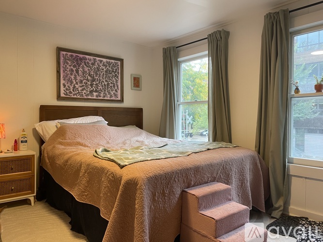 A bedroom with a bed, nightstand, window, and a painting on the wall.