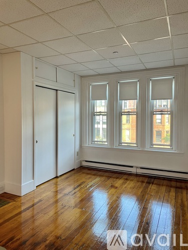 A room with wooden floors and white walls, with a window showing a view of a building outside.