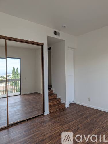 A room with wooden floors and a white wall with a doorway leading to another room.